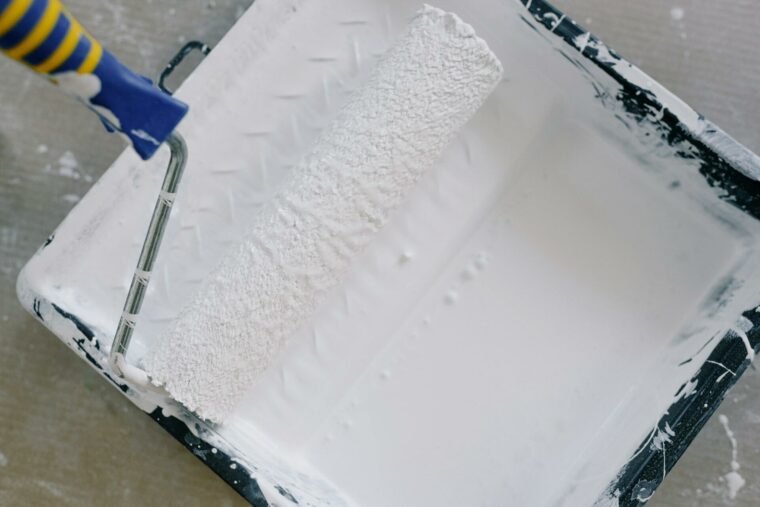 A paint roller is dipped in a paint tray with white paint.