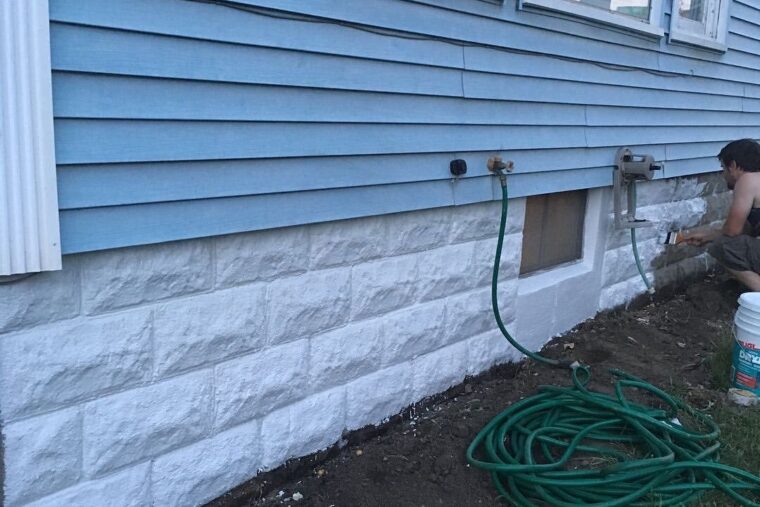 The exterior of a home with white brick and blue vinyl siding. Two garden hoses are connected to the home.