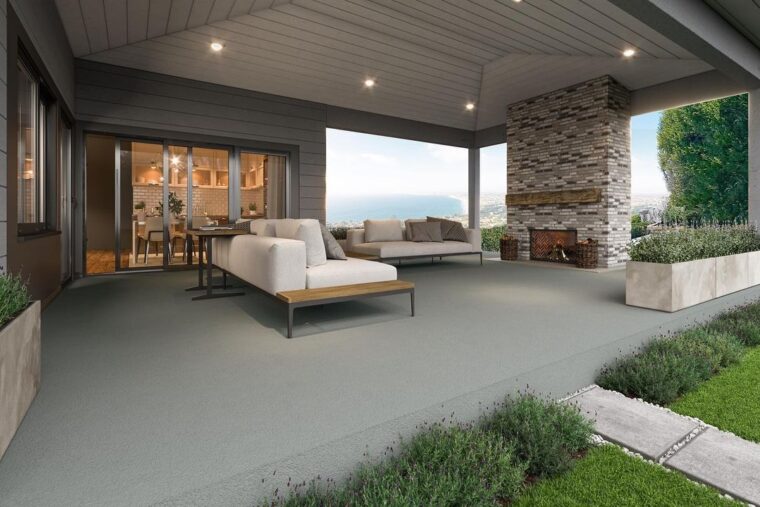 A covered, concrete outdoor living space with white patio furniture and a neutral brick fireplace.