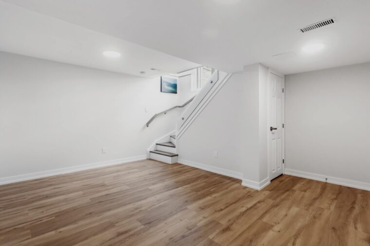 An empty basement with hardwood floors, white walls and bright lighting.