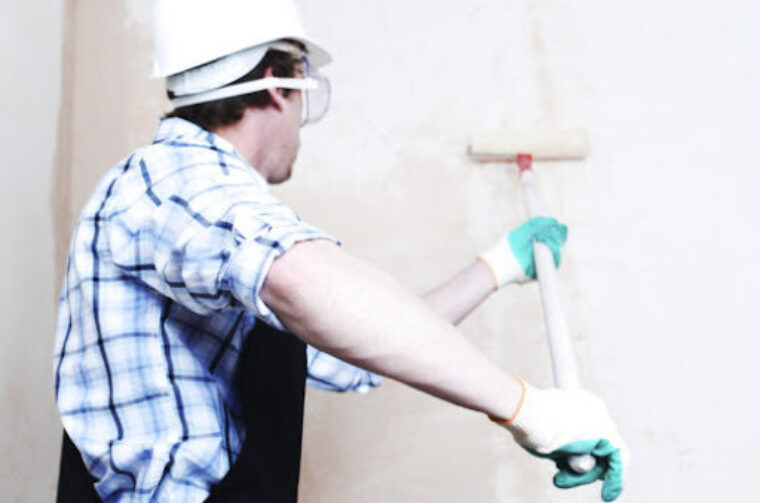 A person in a blue and white flannel applying DRYLOK® Extreme Concrete & Masonry Waterproofer to a wall.