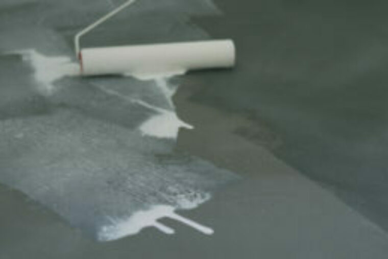 A paint roller is being used to apply a waterproofing solution to concrete flooring.