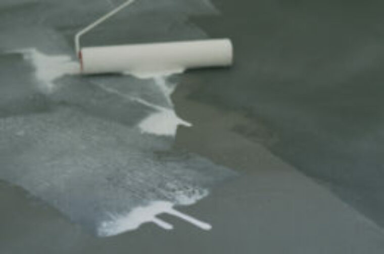 A paint roller is being used to apply a waterproofing solution to concrete flooring.